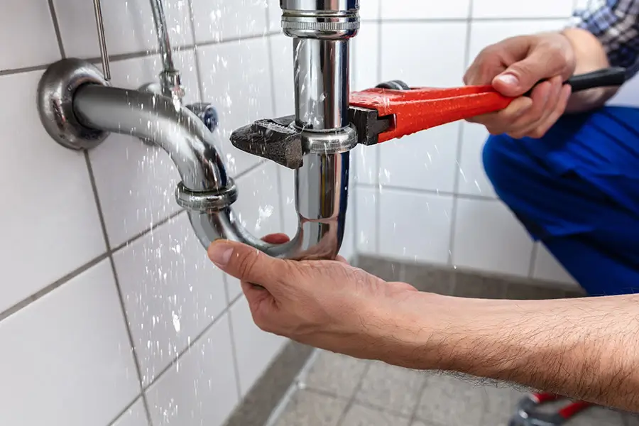 Plumber fixing leaking pipe under sink